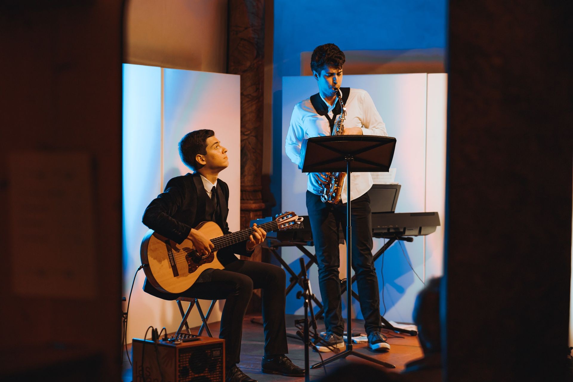 Musicians performing with guitar and saxophone on stage, blue and pink lighting.